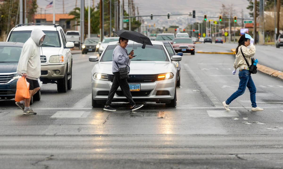 Pedestrians keep dry the best they can while walking along North Eastern Avenue on Tuesday, Mar ...