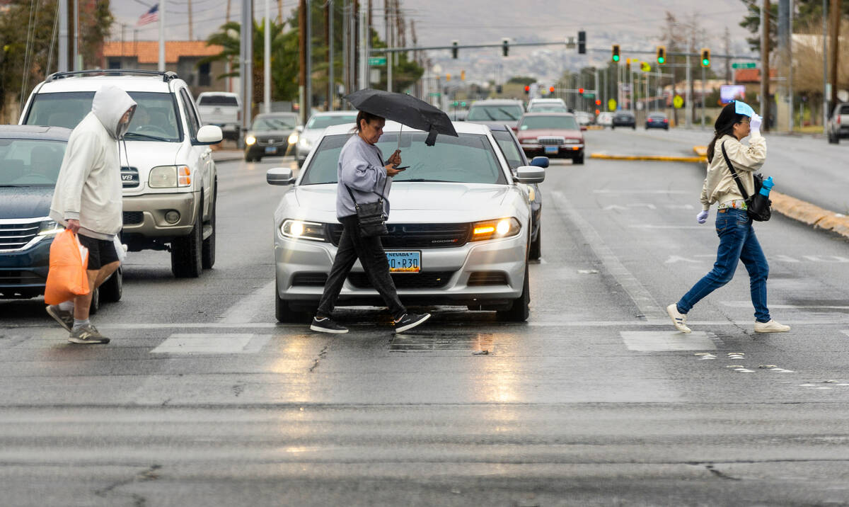Pedestrians keep dry the best they can while walking along North Eastern Ave. as a storm system ...