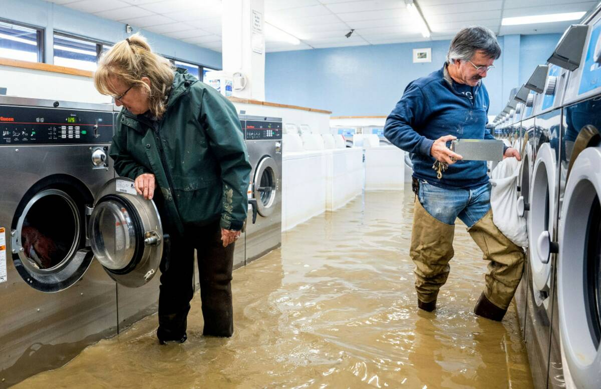 Pamela and Patrick Cerruti empty coins from Pajaro Coin Laundry as floodwaters surround machine ...