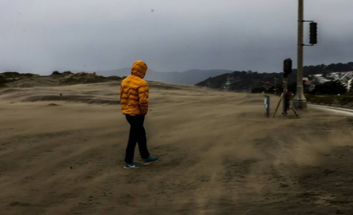 A man walks through a windstorm at Ocean Beach on a stormy morning in San Francisco on Tuesday, ...