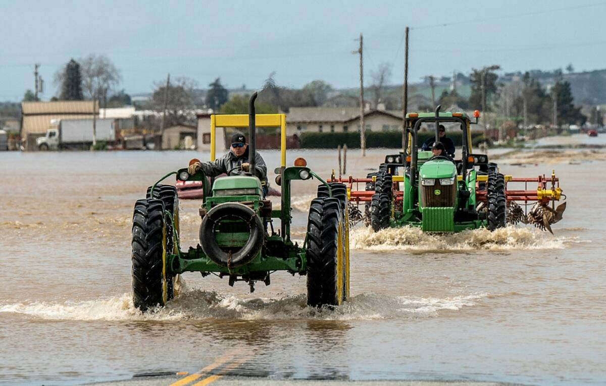 Farm machinery drives through floodwaters in the community of Pajaro in Monterey County, Calif. ...