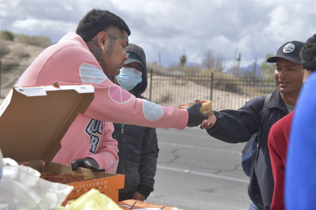 Christopher Ramirez, left, gives pizza to a man near Main Street and Owens Avenue on Saturday, ...