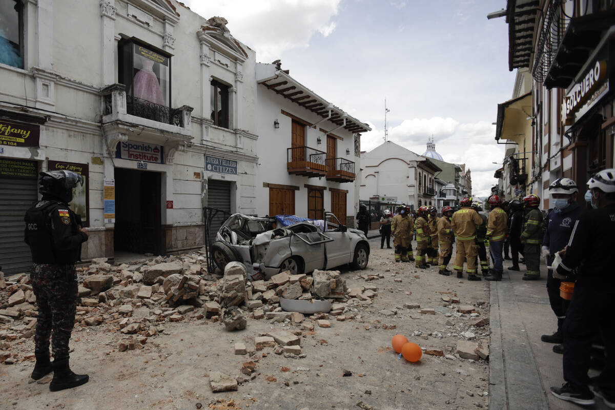 Rescue workers stand next to a car crushed by debris after an earthquake in Cuenca, Ecuador, Sa ...