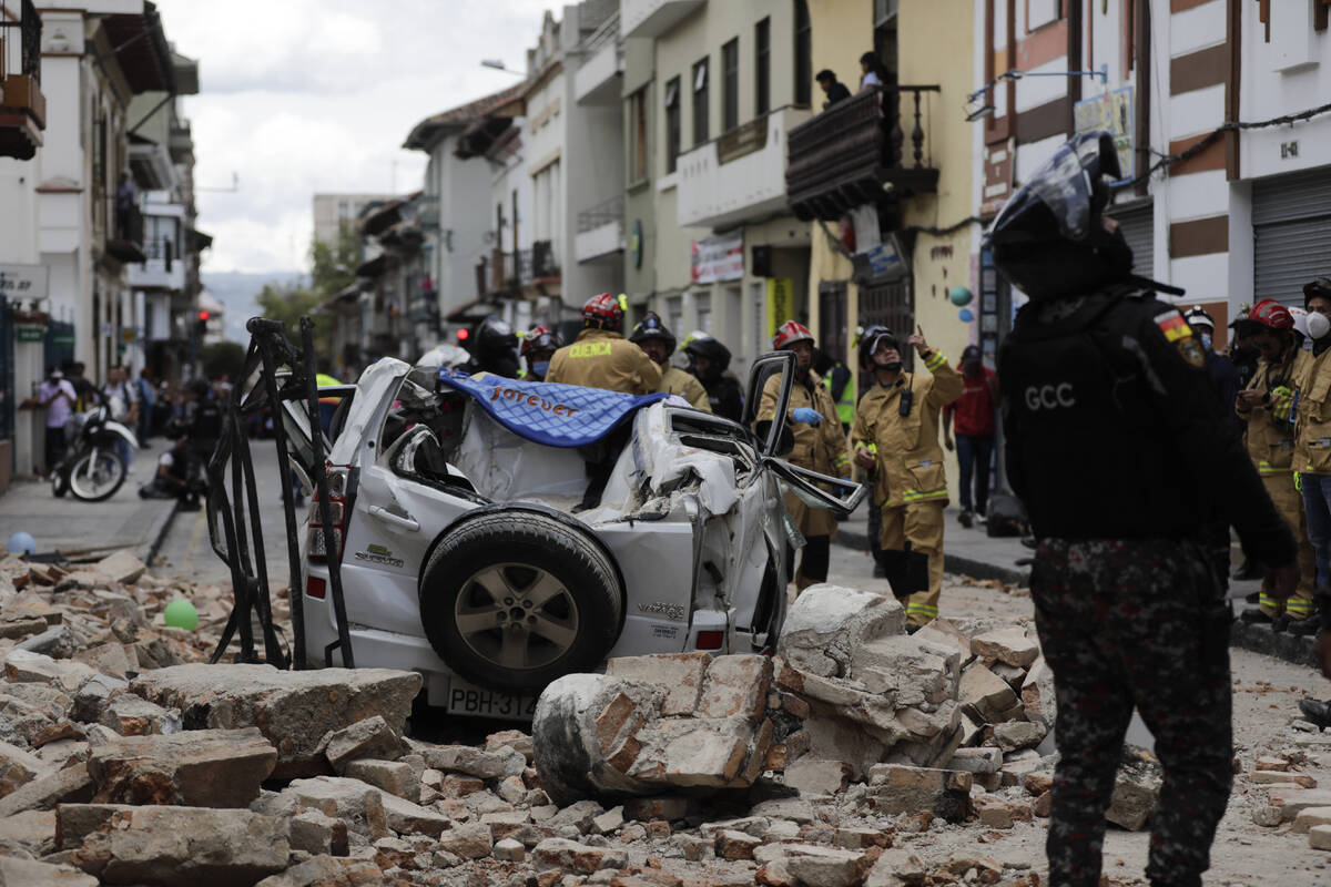 A police officer looks up next to a car crushed by debris after an earthquake shook Cuenca, Ecu ...