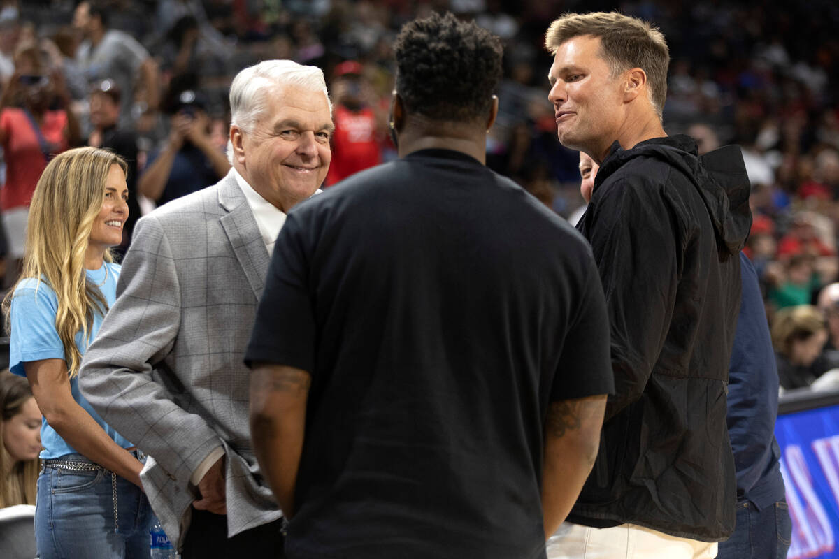 Gov. Steve Sisolak and football quarterback Tom Brady converse with a group during halftime of ...