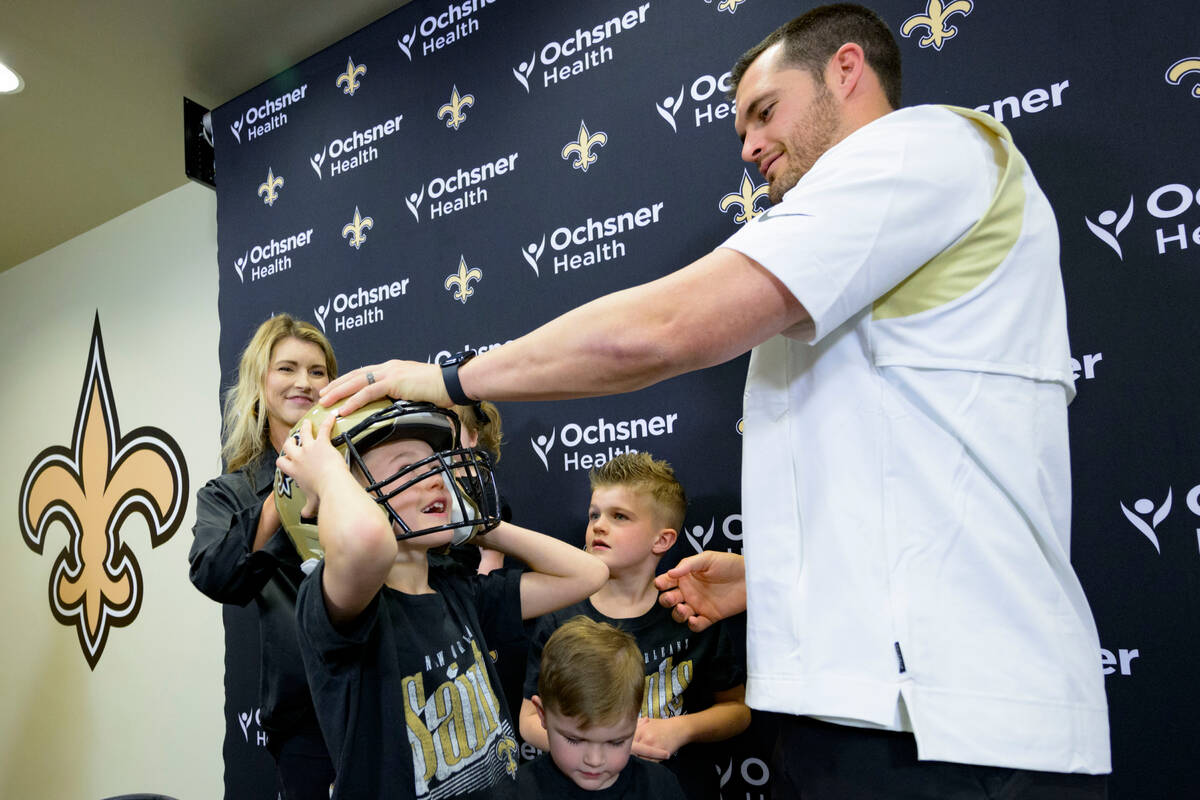 Derek Carr puts a Saints helmet on his son, Dallas Carr, as his wife Heather Carr, left, and ot ...