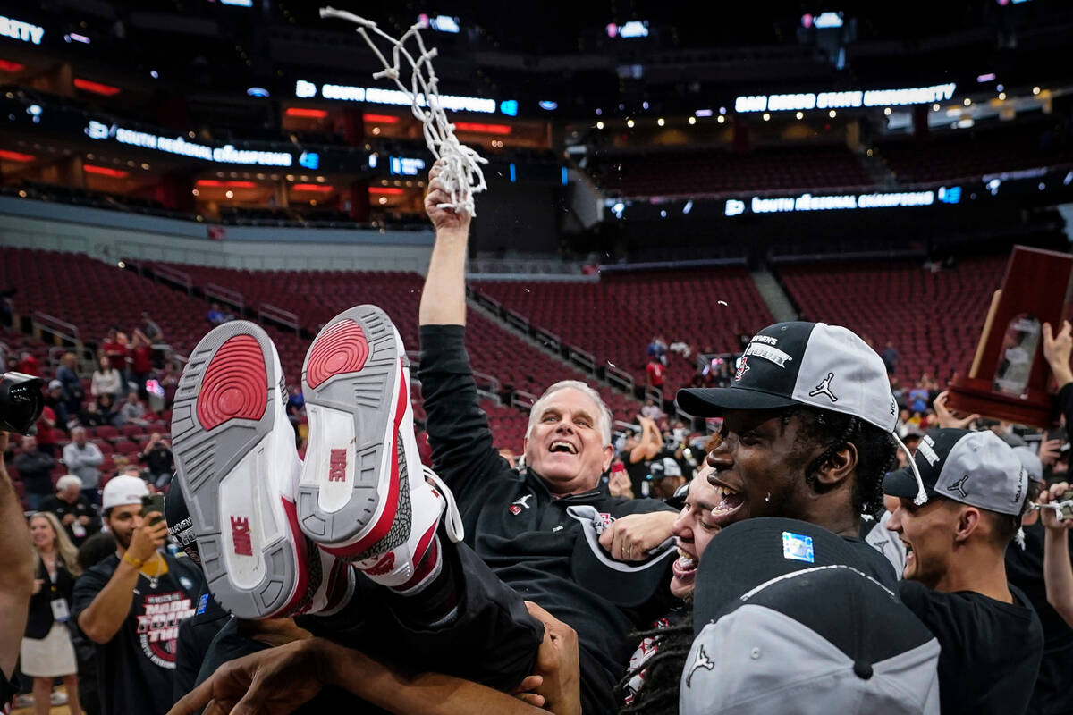 San Diego State head coach Brian Dutcher holds the remains of the net and is hoisted in the air ...