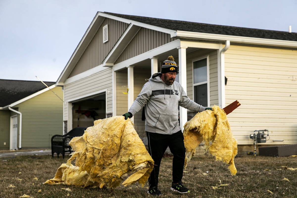 Allen Moore of Hills, Iowa carries large pieces of insulation from the yard of a neighbor's hom ...