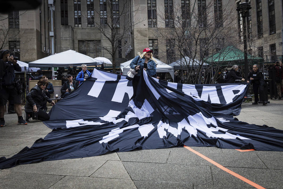 A supporter of former President Donald Trump pulls up an anti-Trump banner off the ground at th ...