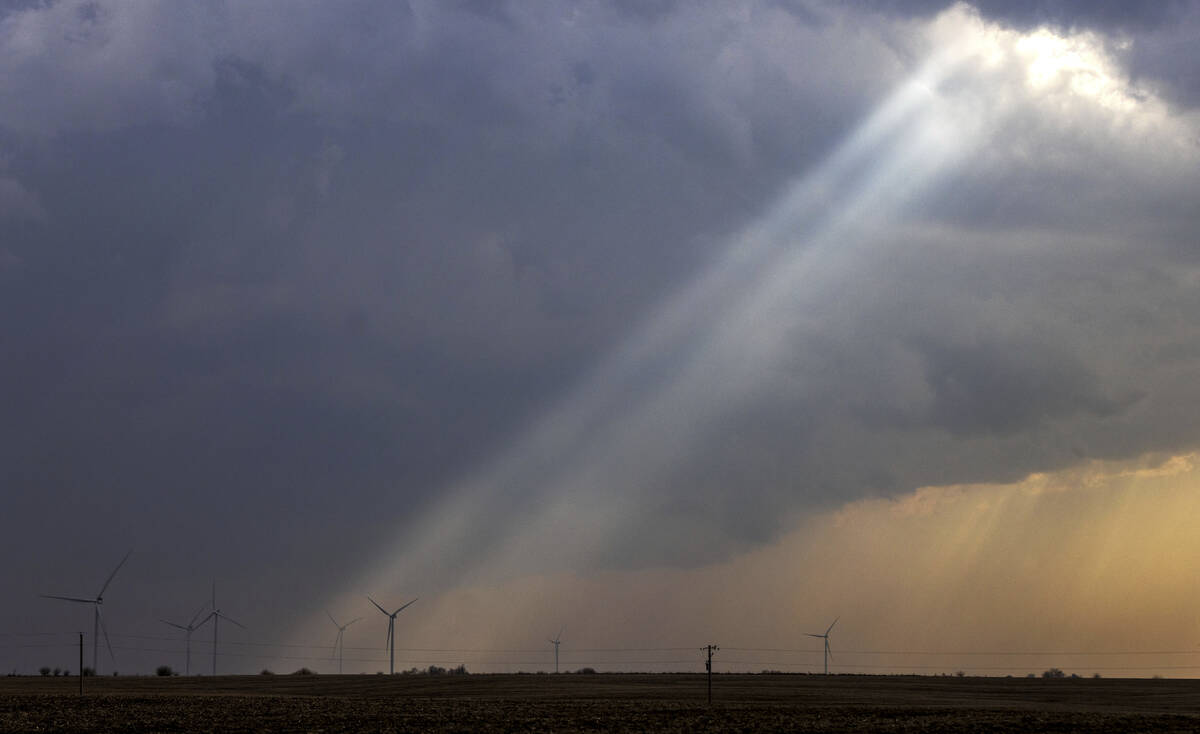Sunlight filters through storm clouds onto a wind turbine as severe weather rolls through the m ...