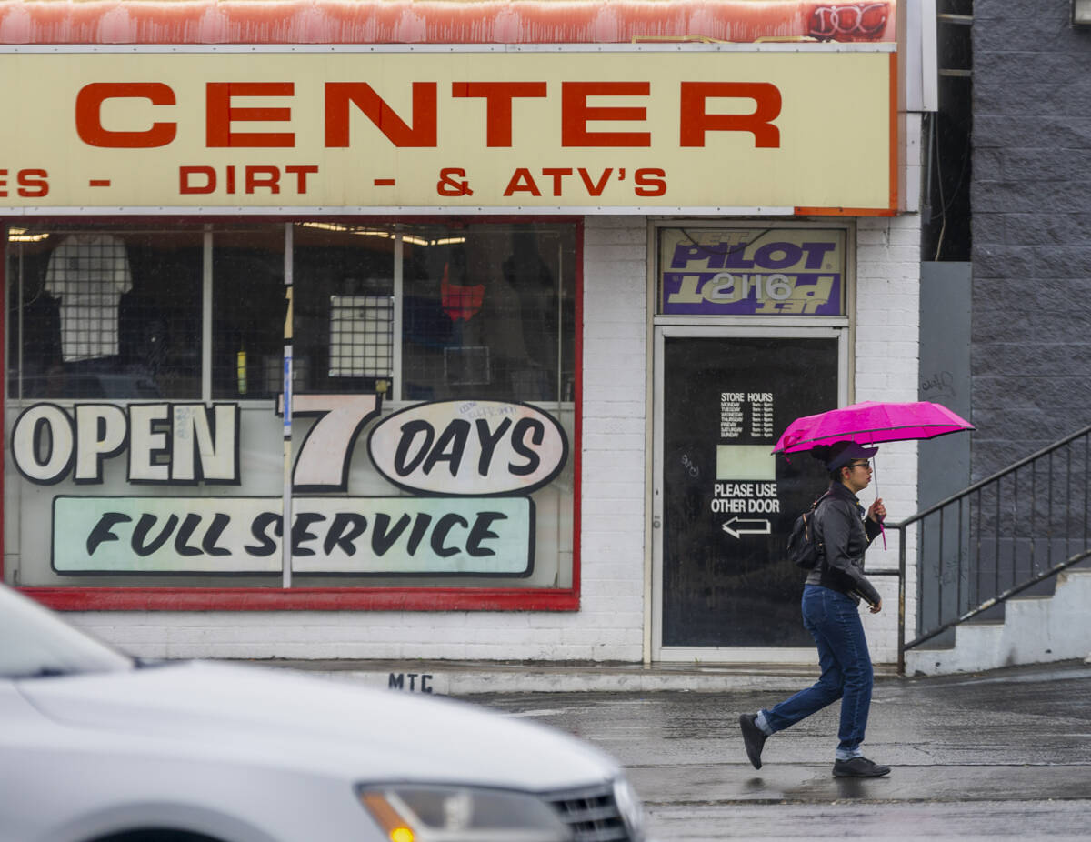 A pedestrian keeps dry under her umbrella as she walks along East Charleston Boulevard as a sto ...