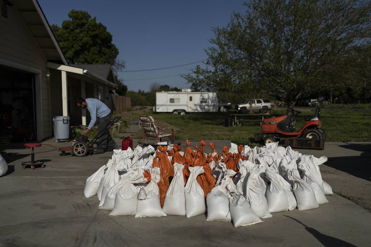 Brennon Williams operates a lawn mower at his girlfriend's home as sandbags are prepared in ant ...