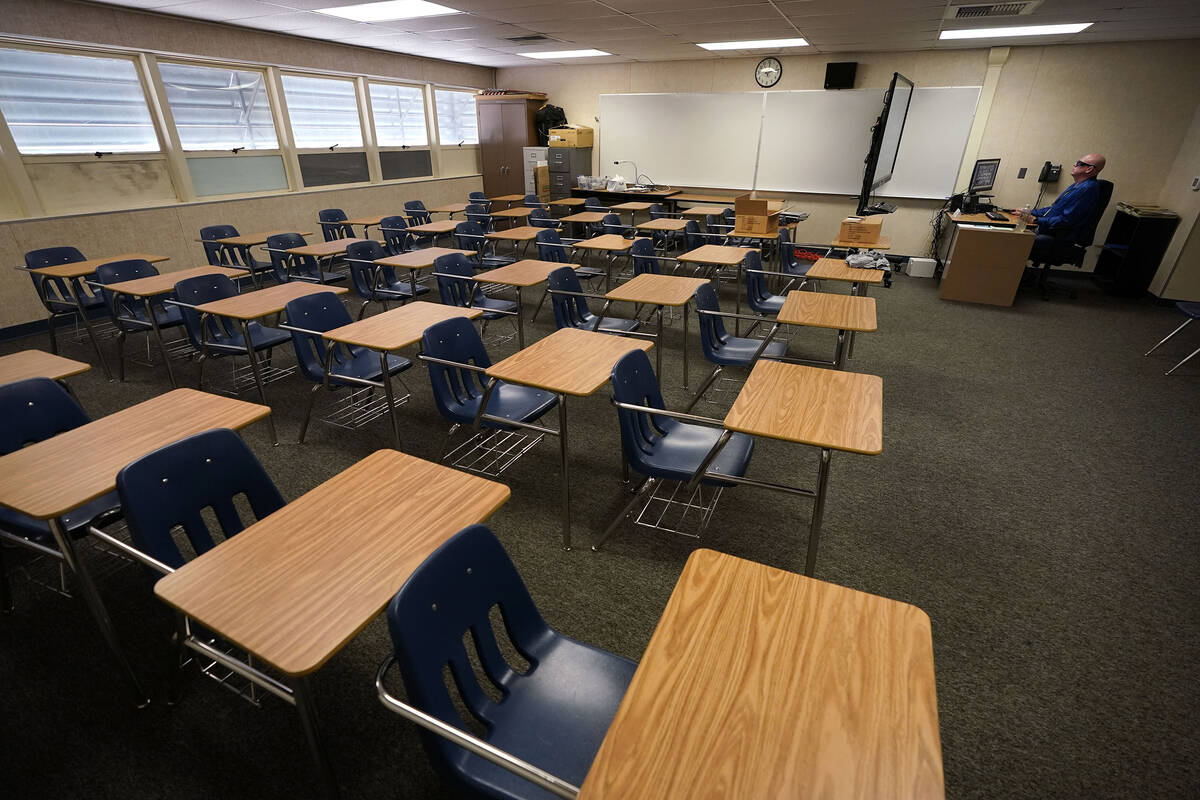 Math teacher Doug Walters sits among empty desks as he takes part in a video conference with ot ...