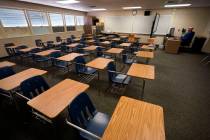 Math teacher Doug Walters sits among empty desks as he takes part in a video conference with ot ...