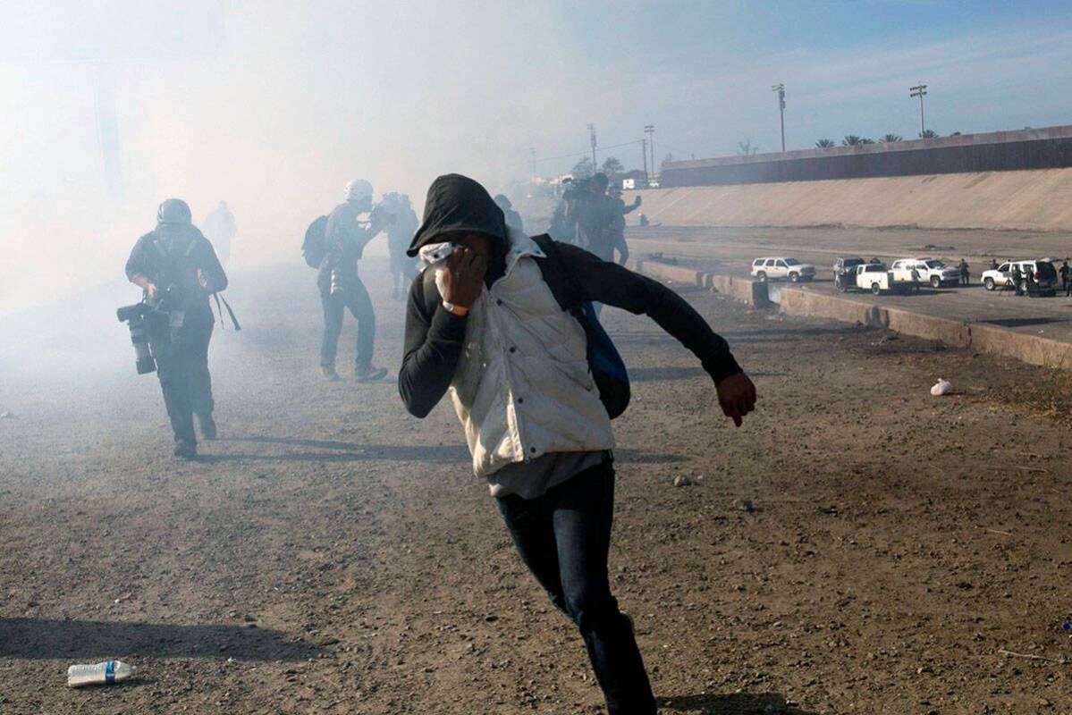 A migrant runs from tear gas launched by U.S. agents, amid members of the press covering the Me ...