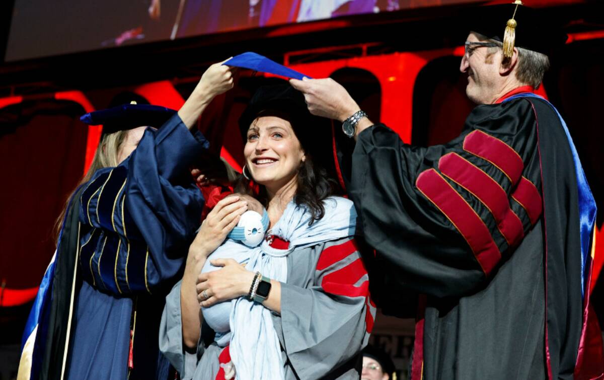 Kristen Herlosky, center, receives her hood from Alyssa Crittenden, dean of Graduate College, a ...