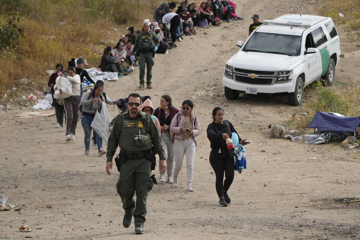 A U.S. Border Patrol agent leads a line of women to a van as they wait to apply for asylum betw ...