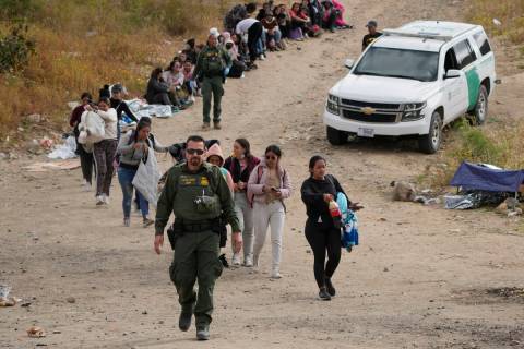 A U.S. Border Patrol agent leads a line of women to a van as they wait to apply for asylum betw ...