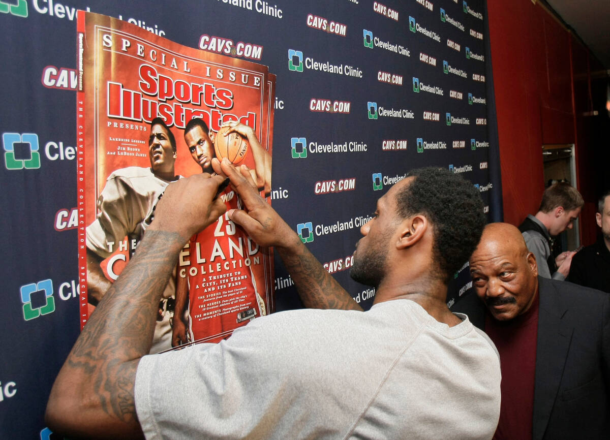 FILE - Cleveland Cavaliers' LeBron James, left, signs a copy of a Sports Illustrated cover as f ...