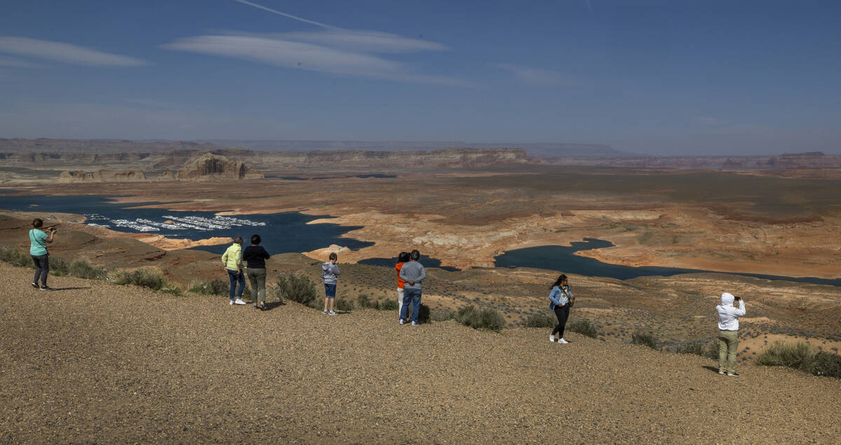 Visitors stand above and look at the declining expanse of Lake Powell as it feeds into the Colo ...
