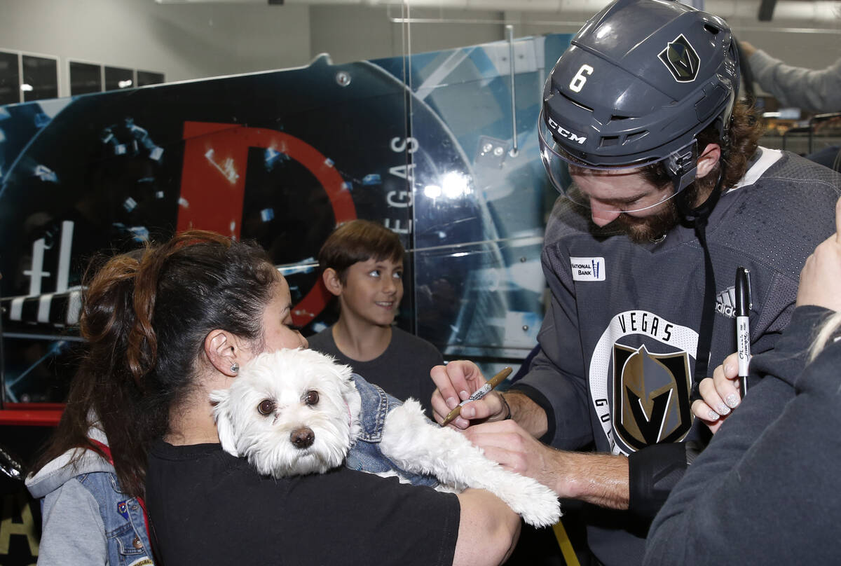 Golden Knights defenseman Colin Miller signs an autograph on the collar of Julissa Garcia's dog ...