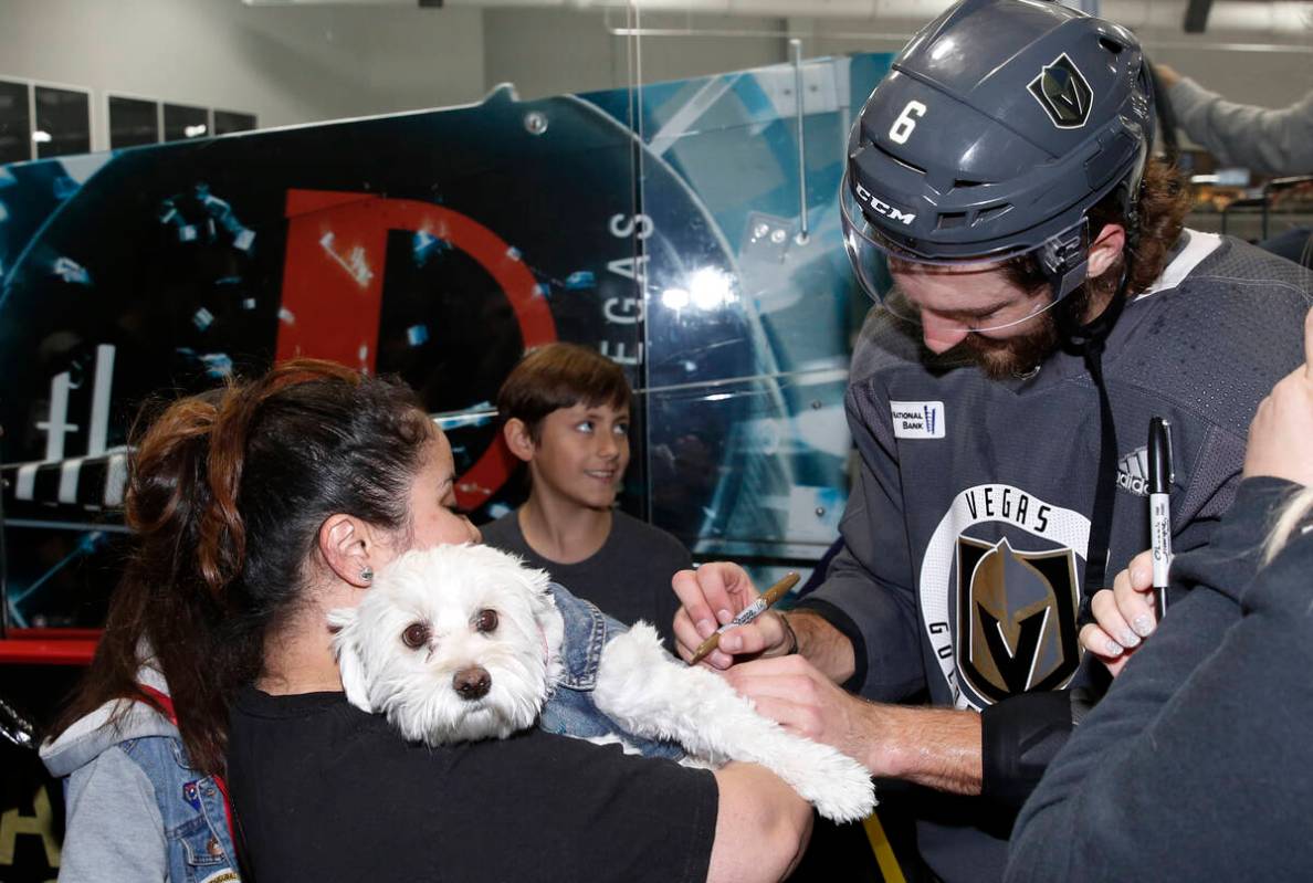 Golden Knights defenseman Colin Miller signs an autograph on the collar of Julissa Garcia's dog ...