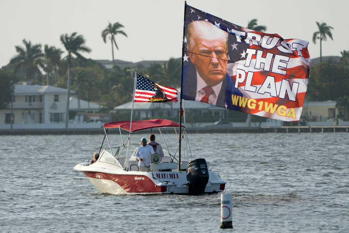 Supporters of former President Donald Trump fly a flag from a boat reading "Trust the Plan ...