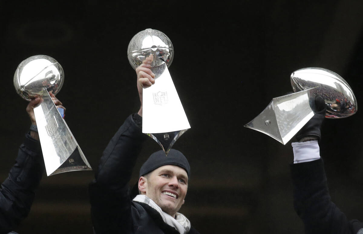Then-New England Patriots quarterback Tom Brady holds a Super Bowl trophy, between others the t ...