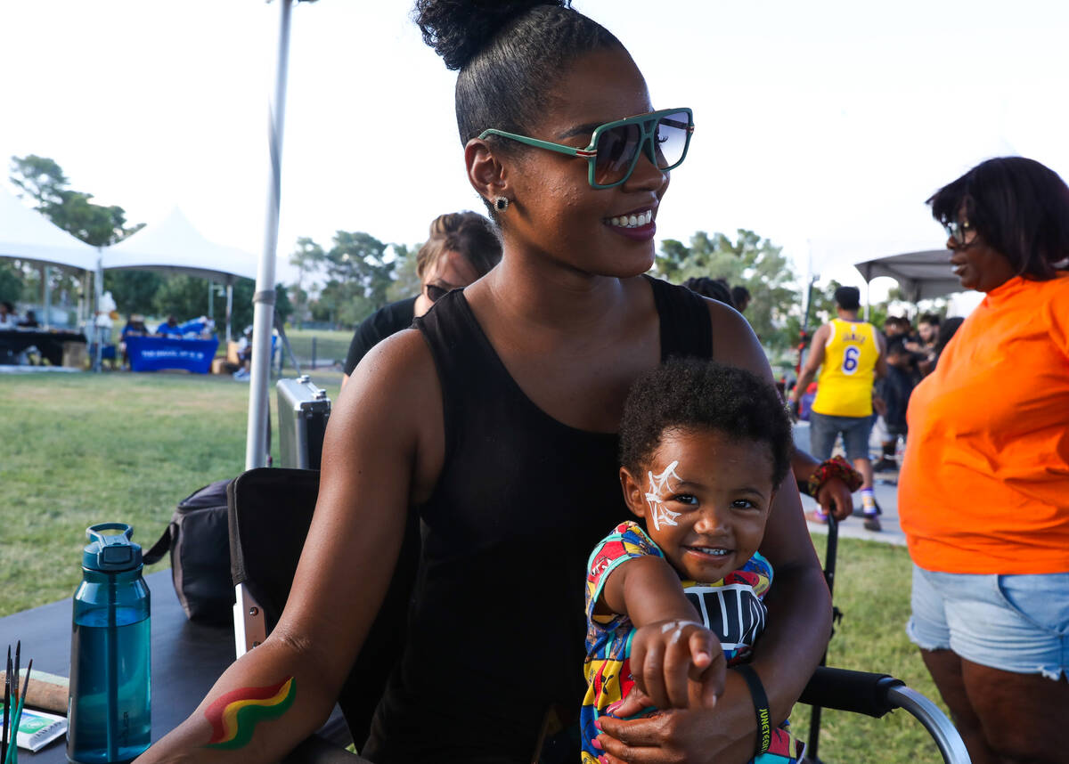 Lashea Warren holds Dominic Butts, 2, as he gets his face painted at the F.A.I.T.H Juneteenth F ...