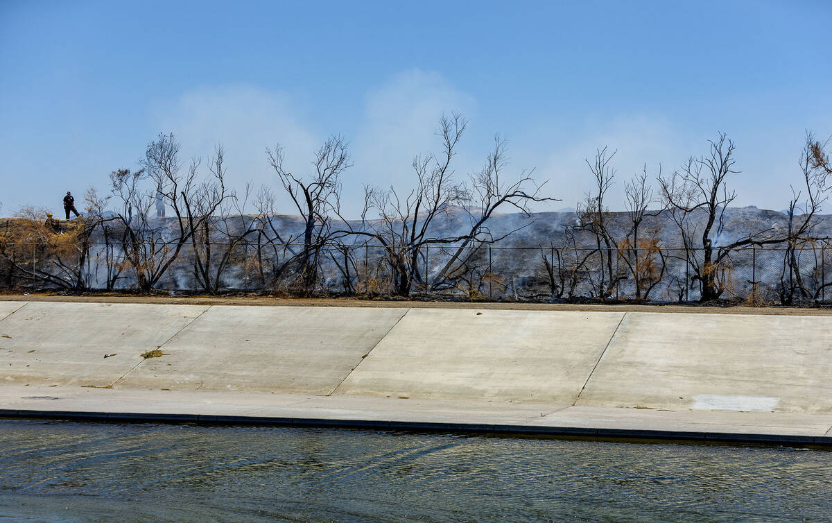 Clark County firefighters extinguish a brush fire adjacent to the Las Vegas Wash along the far ...