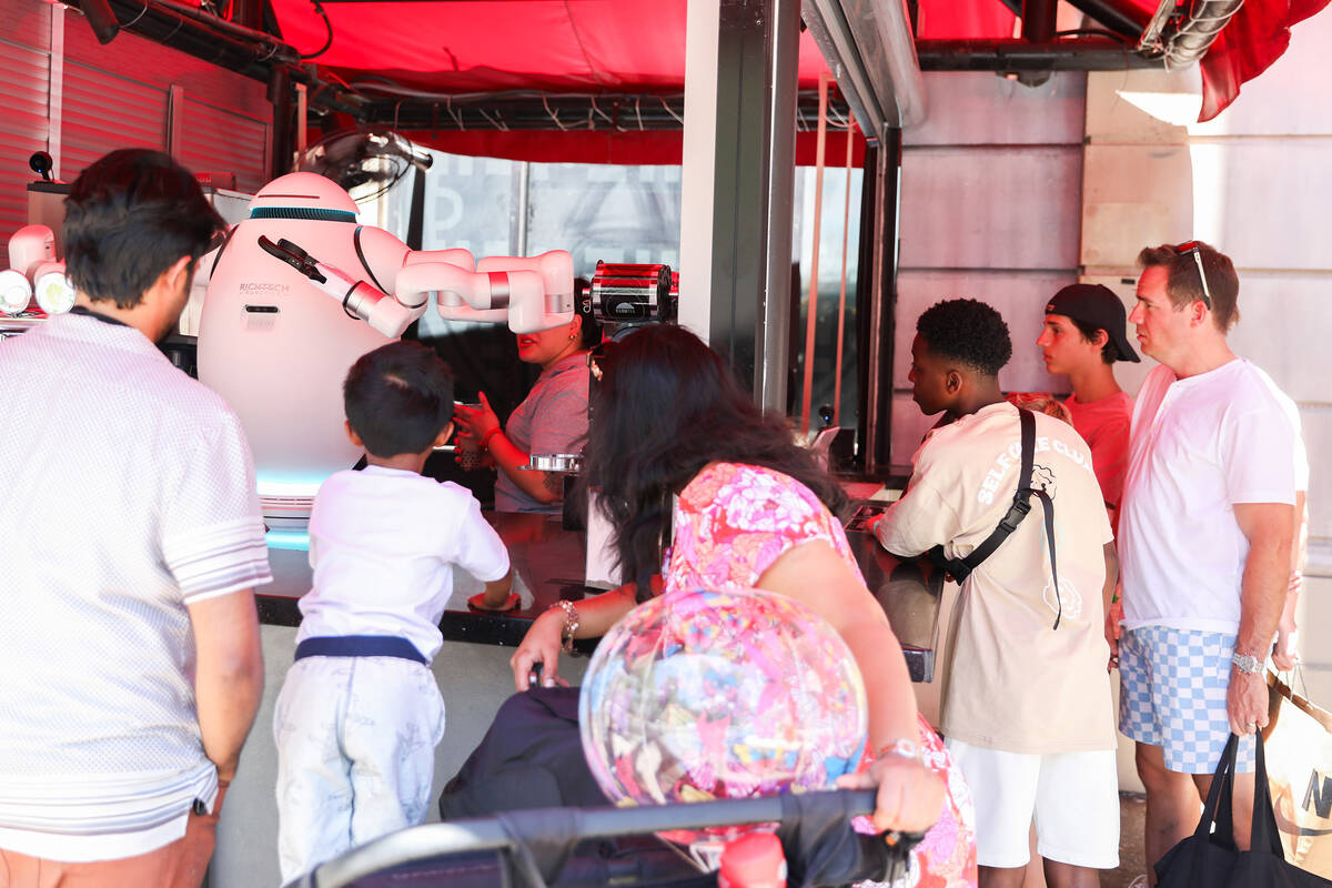 A crowd of customers watches in wonder as Adam the robot prepares their drinks at Cloutea, the ...