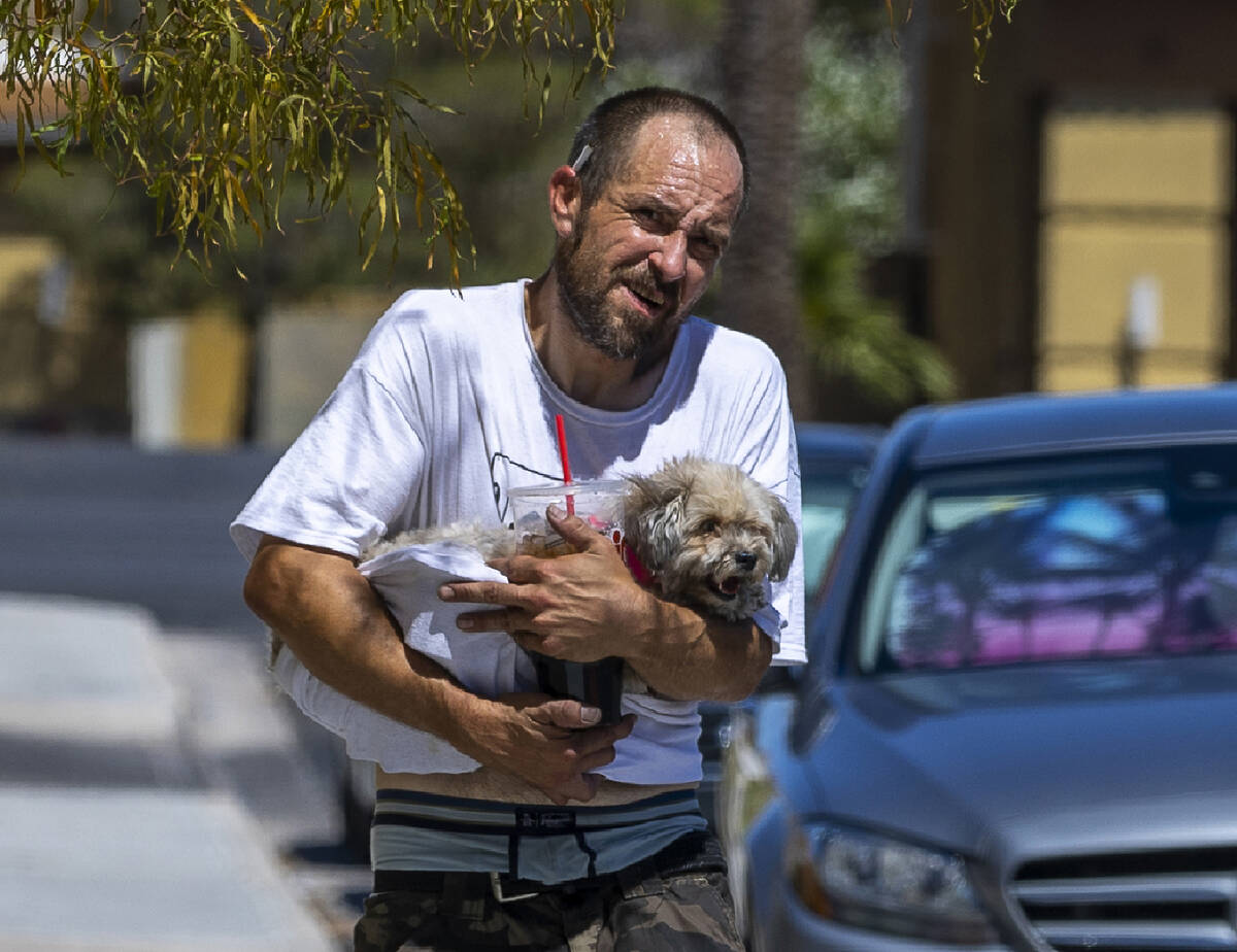 Jimmie Jones carries his dog Sunshine due to the searing pavement along with cold drinks along ...
