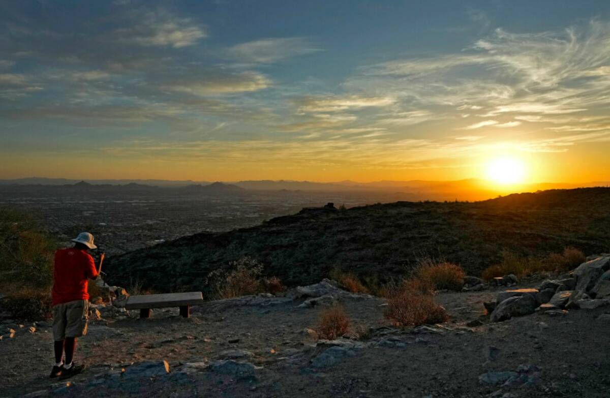 A hiker photographs the sun rising over the Valley atop South Mountain, Monday, July 17, 2023 P ...