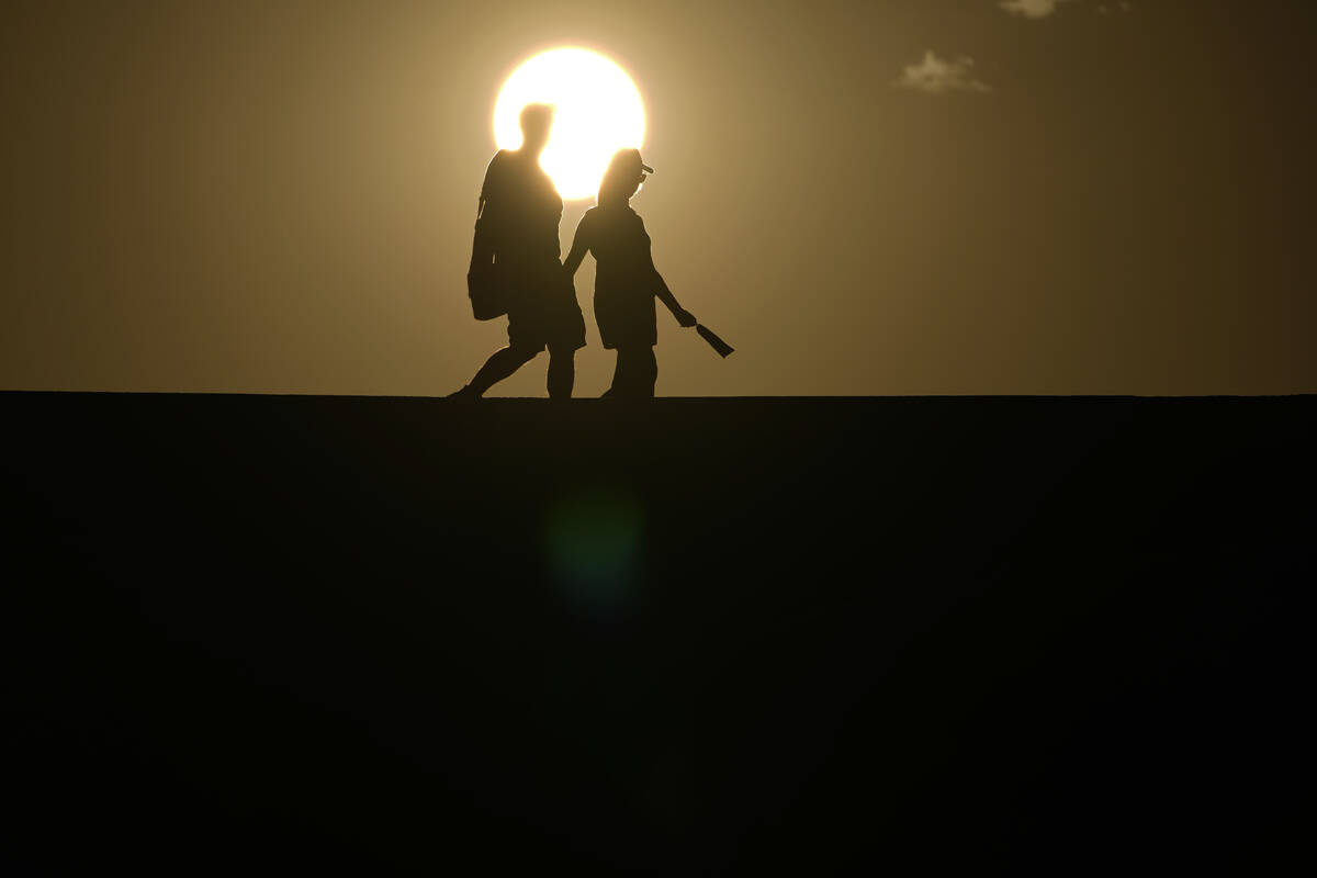 FILE - People walk along a trail as the sun sets, Sunday, July 16, 2023, in Death Valley Nation ...