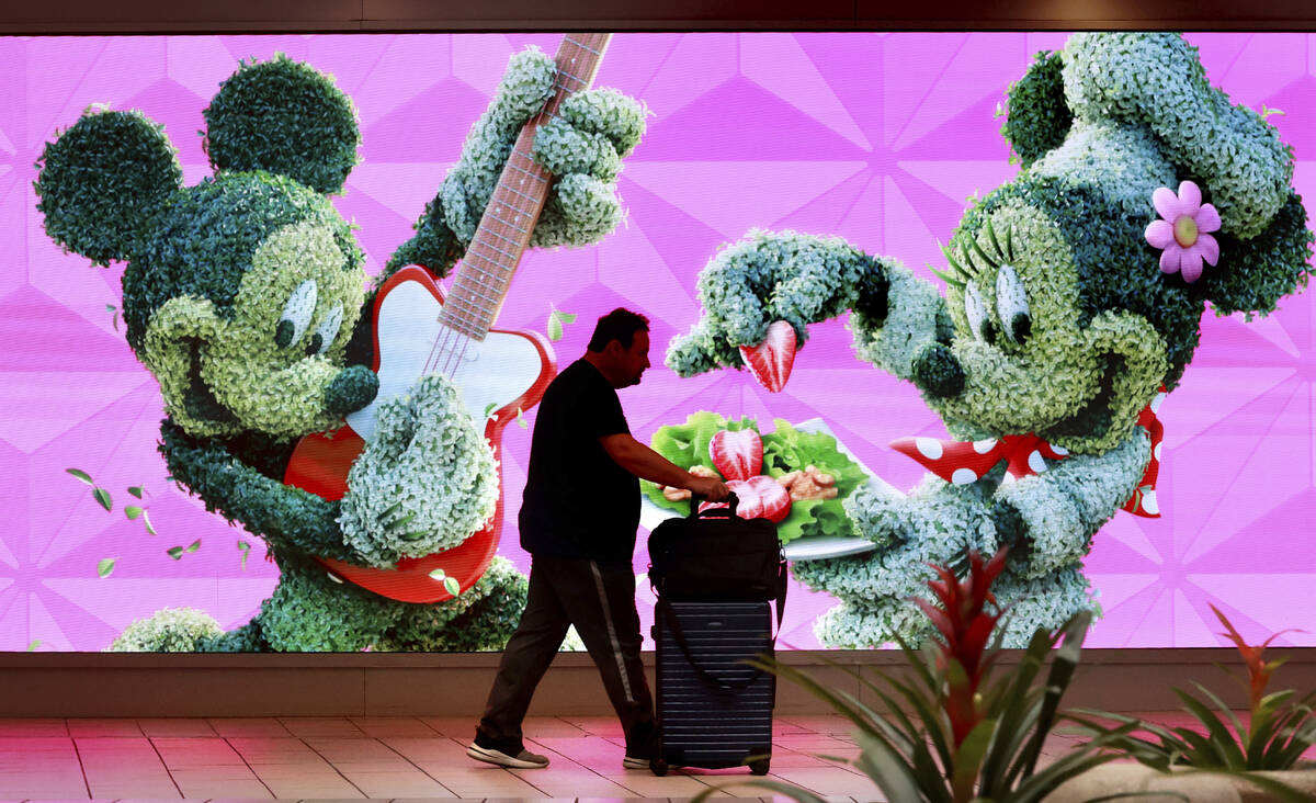A traveler walks past a jumbo screen projecting images of Walt Disney World in the east hall at ...