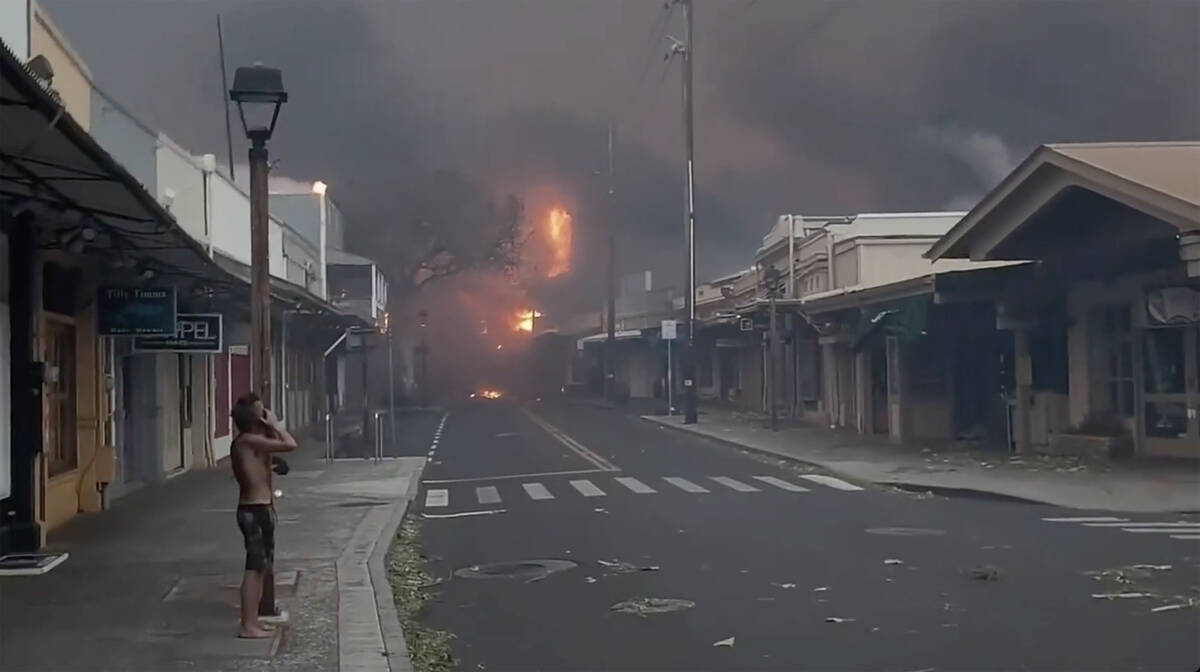People watch as smoke and flames fill the air from raging wildfires on Front Street in downtown ...