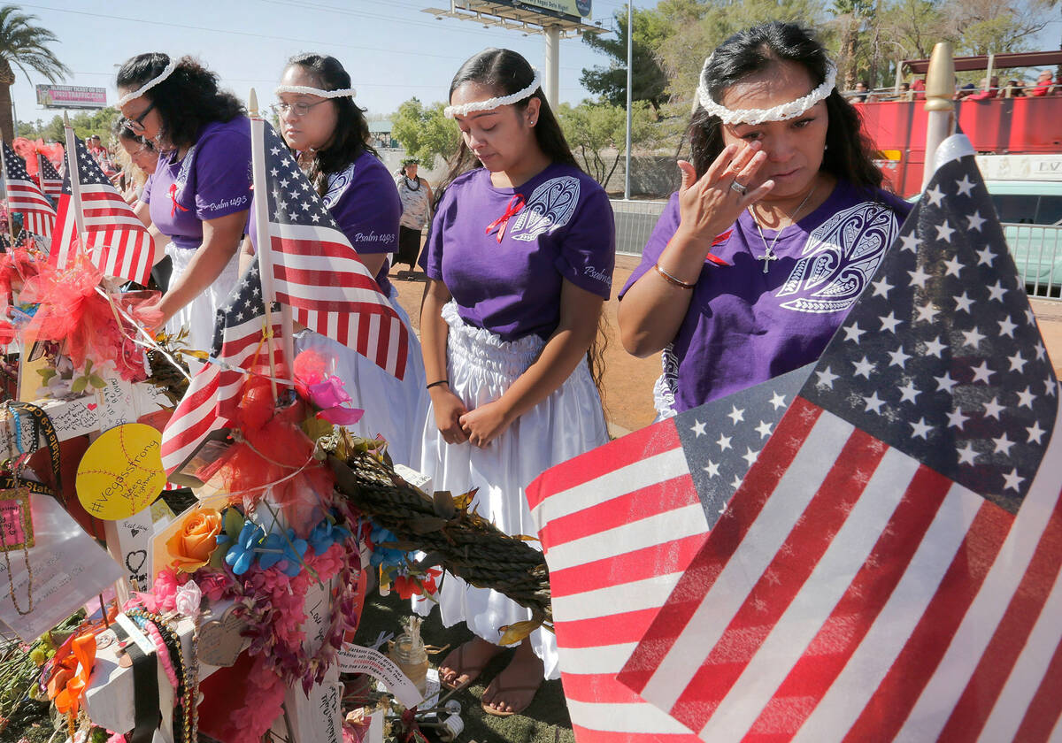 Vilma Valencia of Las Vegas, right, wipes tears after placing ti-leaf lei with other volunteers ...