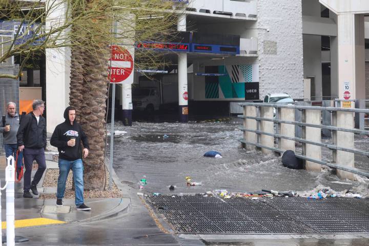 Pedestrians walk by as water flows from The Linq parking garage to a flood channel after rain o ...