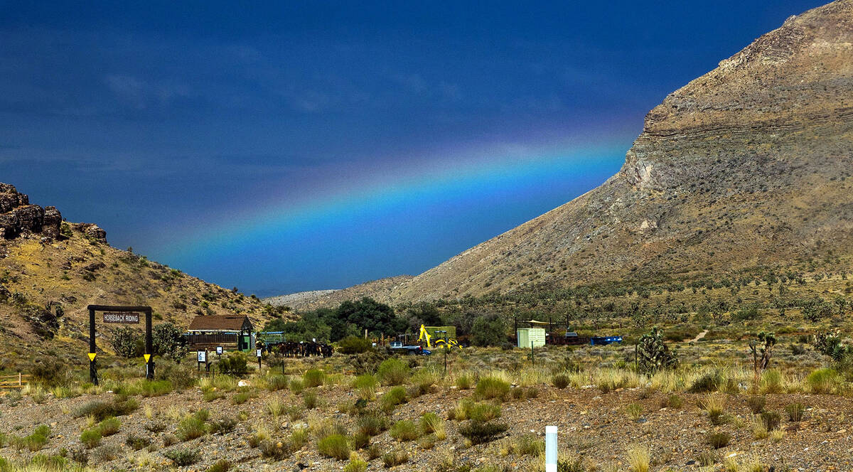 A rainbow stretches across the sky in the distance behind the horseback riding stables within t ...