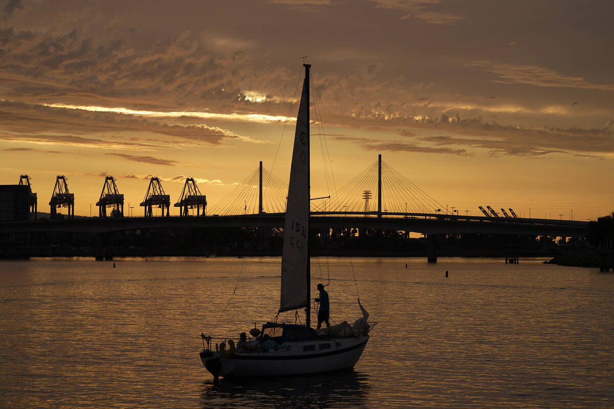 A sailboat prepares to dock as the sun sets over the Long Beach International Gateway ahead of ...