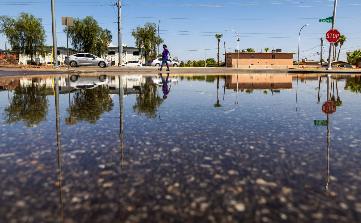 A woman walks along East Sahara Ave. where water remains pooled up near the intersection with S ...