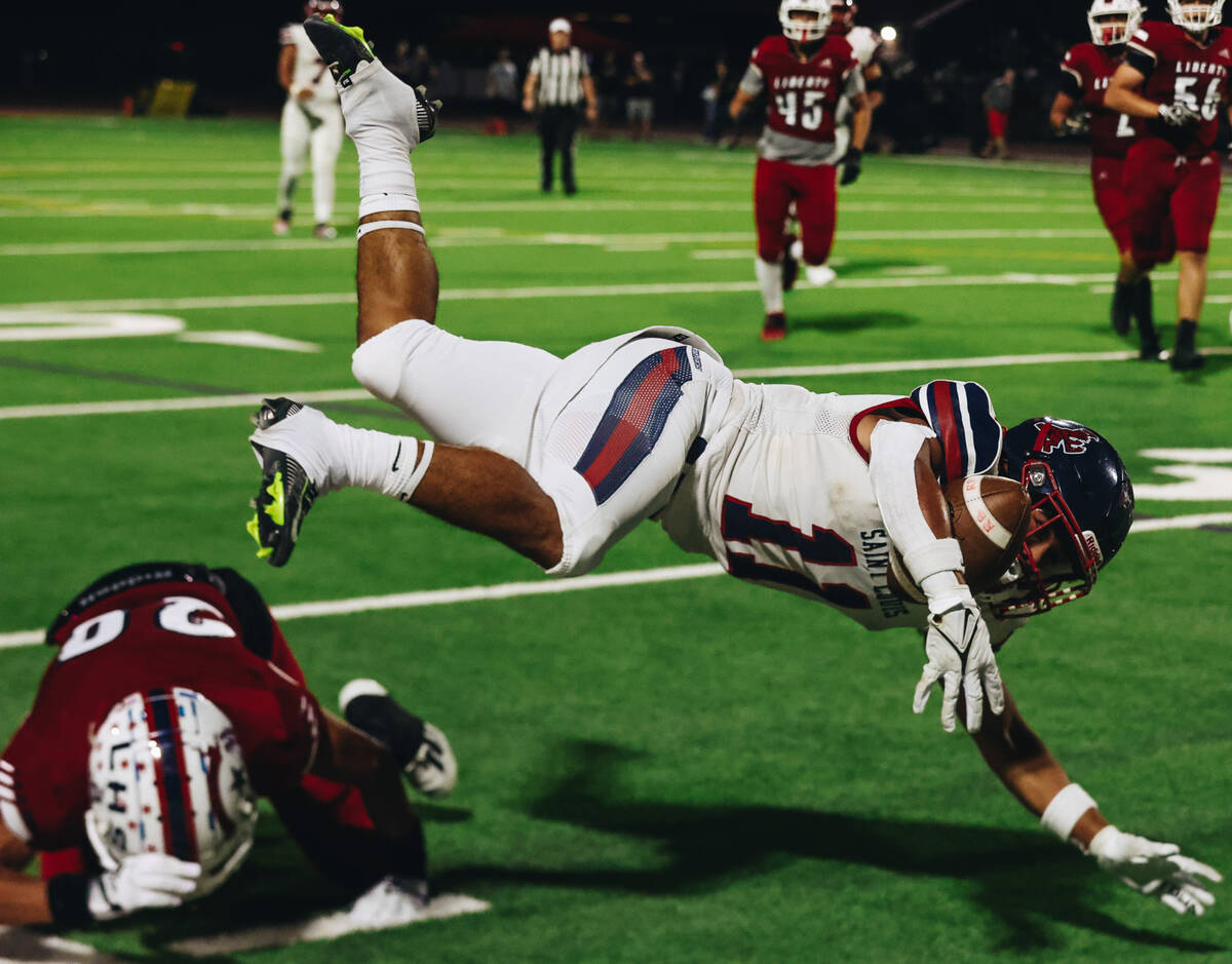 St. Louis slotback Titan Lacaden (11) dives over Liberty cornerback Peyton Caldwell (20) with t ...