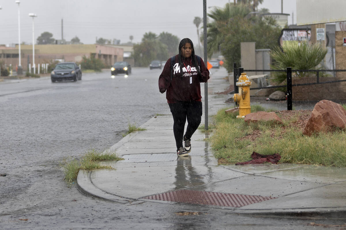 A pedestrian walks through rain at the intersection of East Sahara Avenue and South Bruce Stree ...