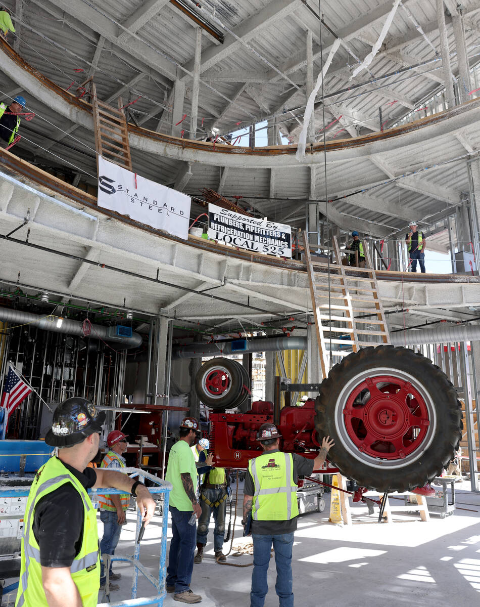 Workers prepare to install an antique tractor on the ceiling of the under construction Blake Sh ...