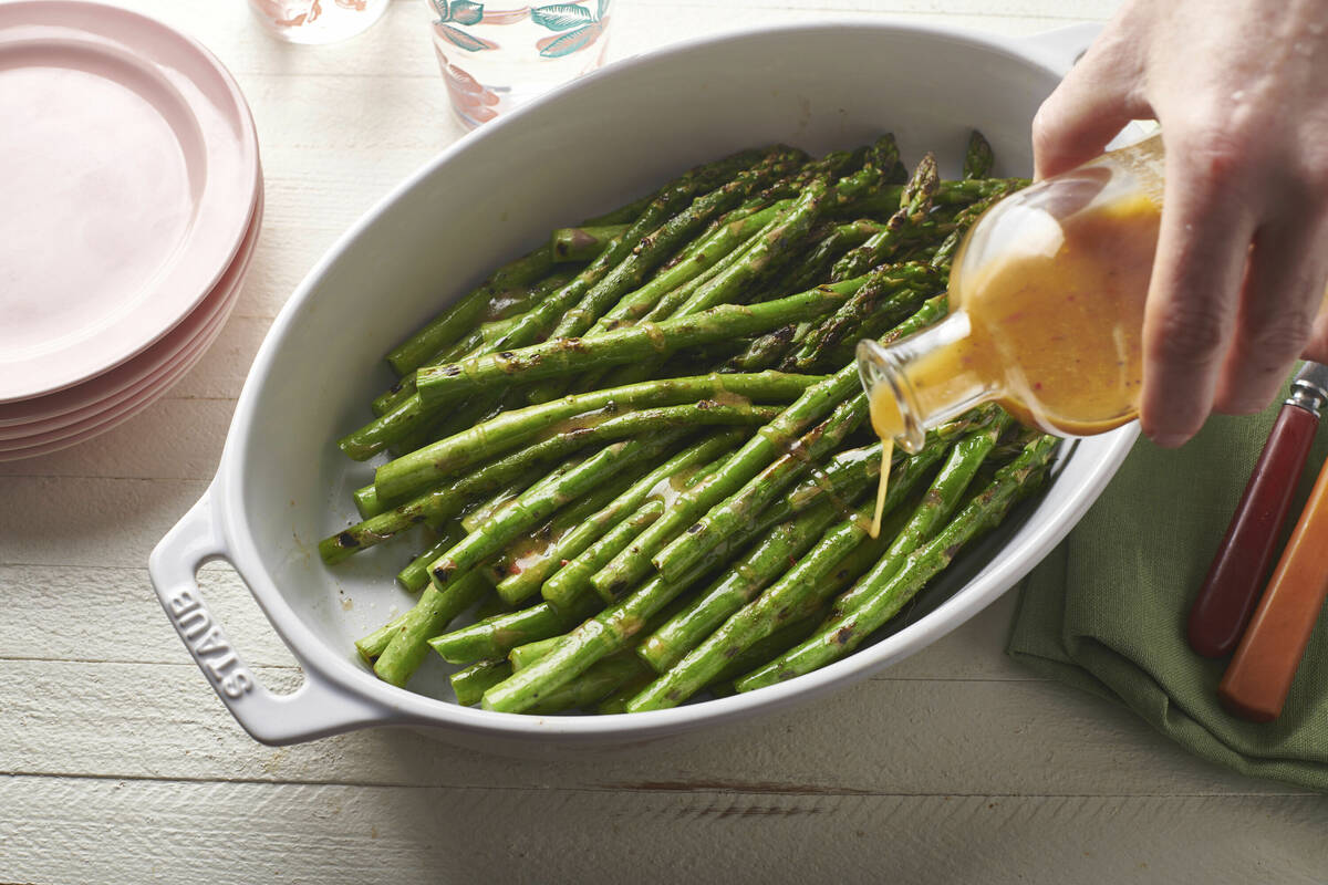 A vinaigrette dressing is poured over grilled asparagus in February 2020. Beyond lettuce salads ...