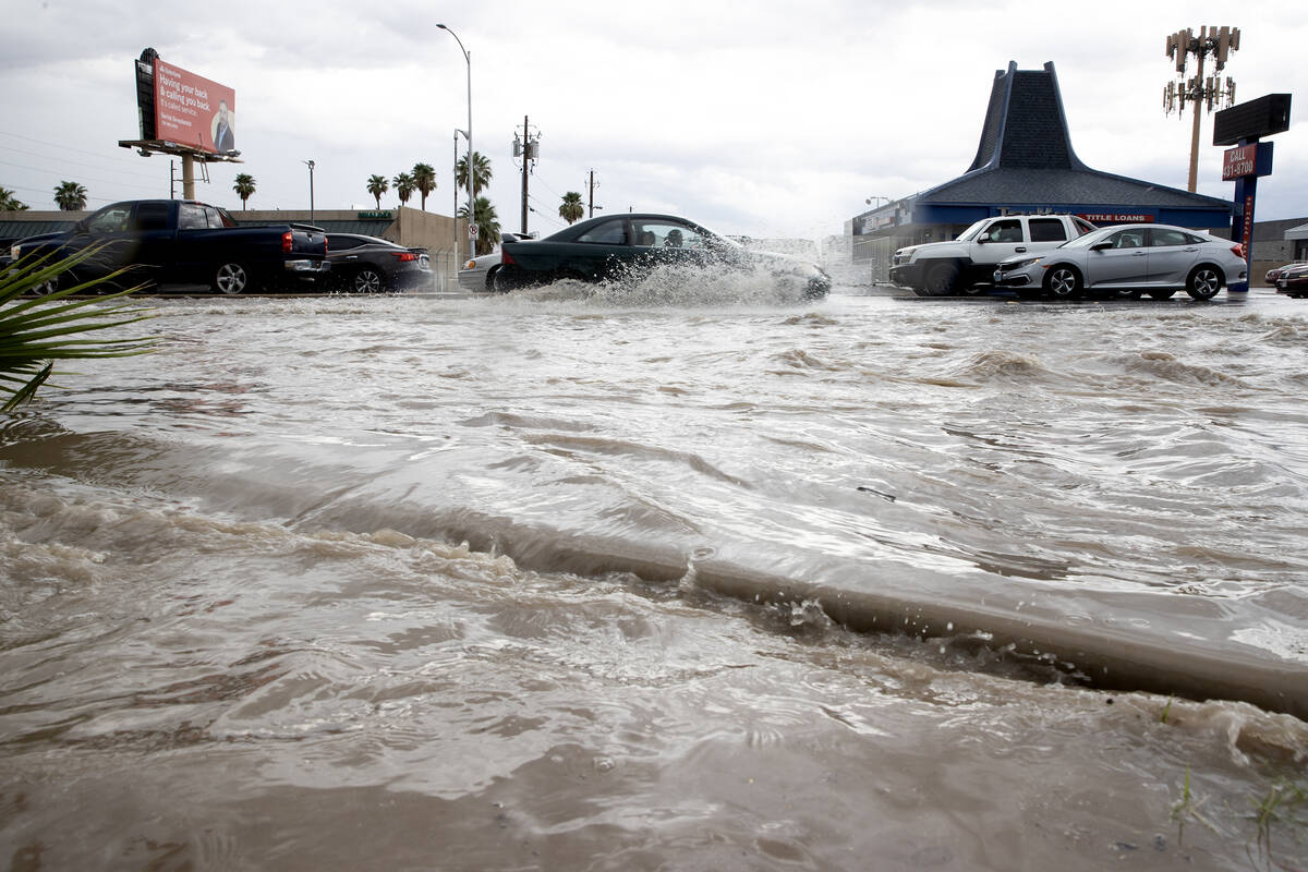 Flash flooding spills over the sidewalk and into a parking lot while traffic plows through the ...