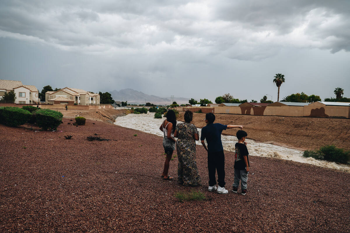 A family watches as Duck Creek floods from recent rainfall near Jack in the Box at East Russell ...