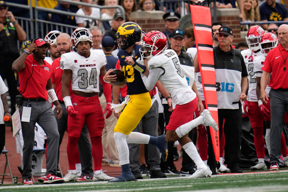 Michigan quarterback Jack Tuttle (13) is pushed out of bounds by UNLV defensive back Cameron Ol ...