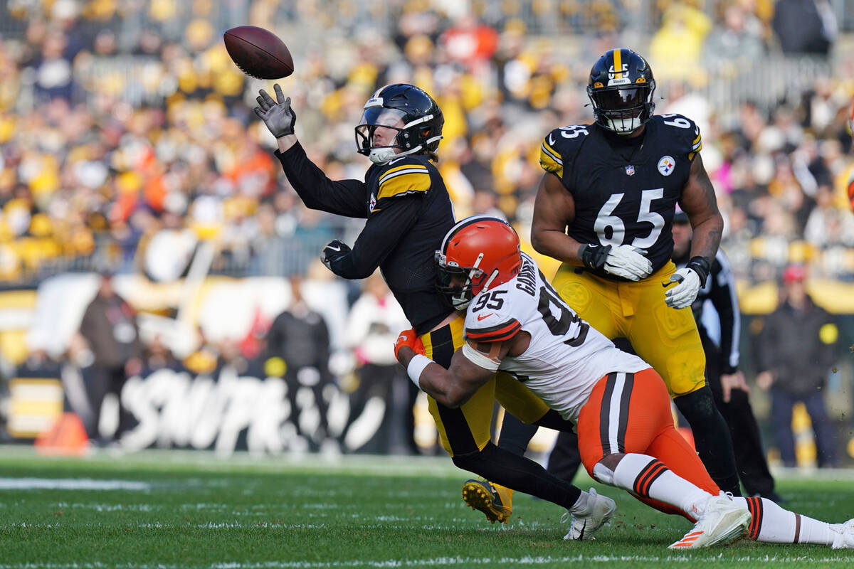 Pittsburgh Steelers quarterback Kenny Pickett, top left, gets off a pass while in the grasp of ...
