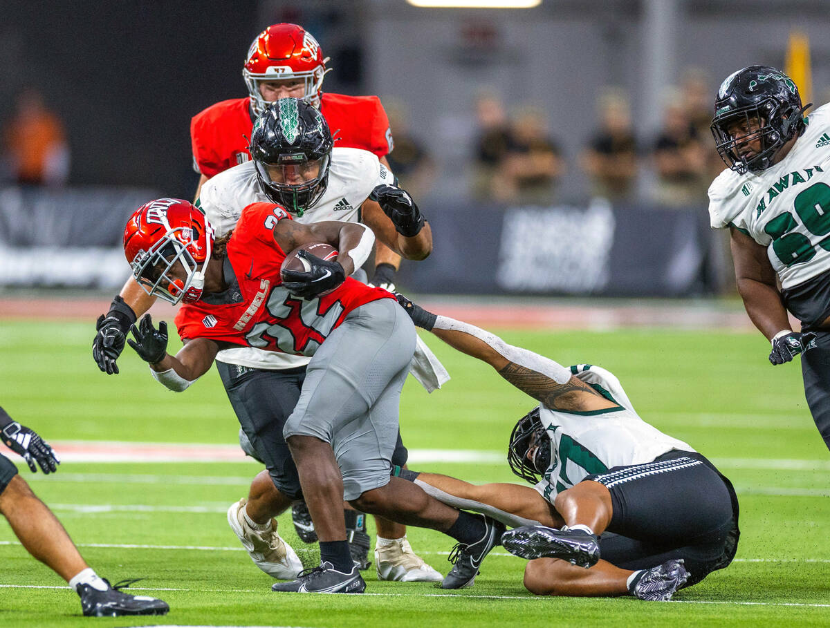 UNLV running back Jai'Den Thomas (22) fights off a tackle from Hawaii linebacker Isaiah Tufaga ...